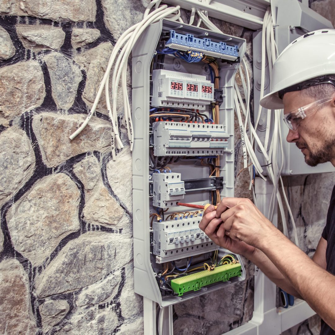 a male electrician works in a switchboard with an electrical connecting cable, connects the equipment with tools, the concept of complex work, space for text